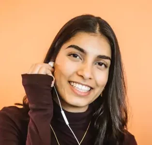 Portret van een lachende vrouw met oortjes in, tegen een oranje achtergrond