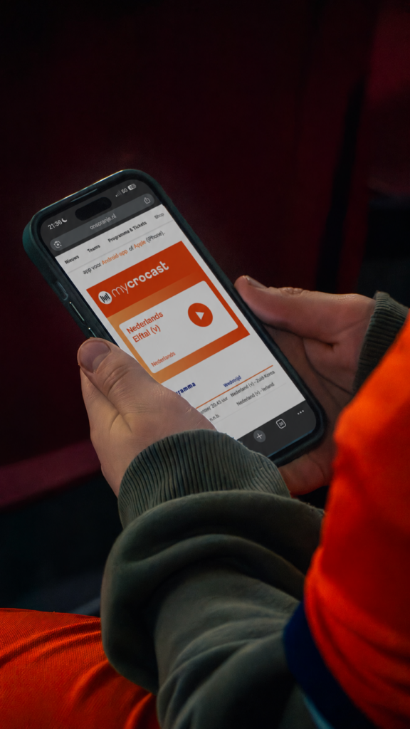 Supporter in het oranje volgt de audiodescriptie op de telefoon in de Mycrocast-app
